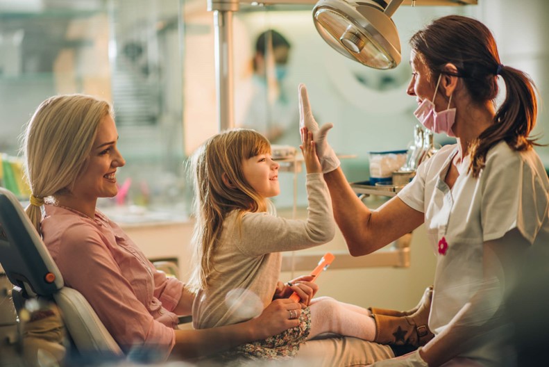 A child on her mothers lap giving a dentist a high five