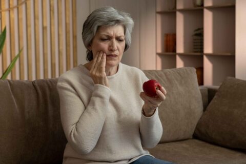 A person holding an apple and experiencing tooth pain