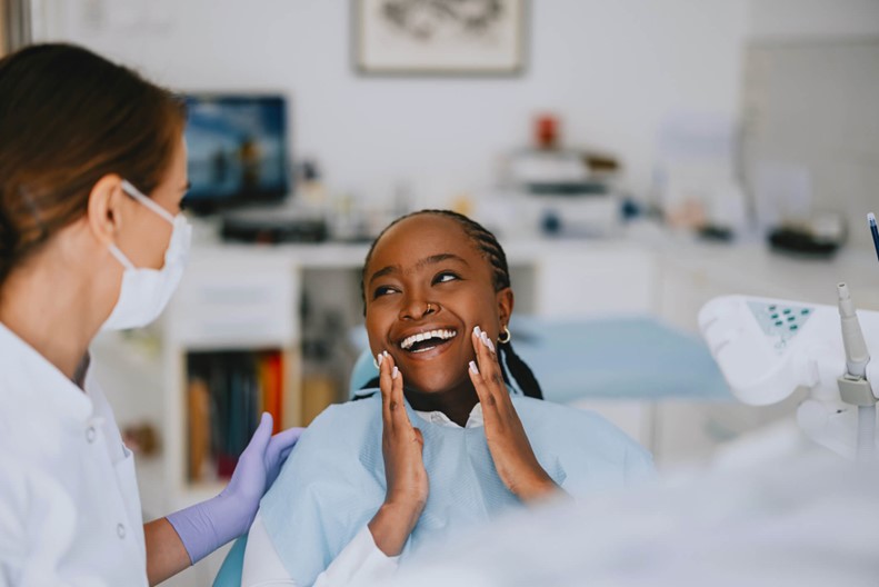 A person in a blue gown holding her face next to a dentist