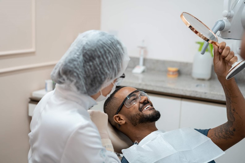 Man looks at teeth in a mirror at the dentist